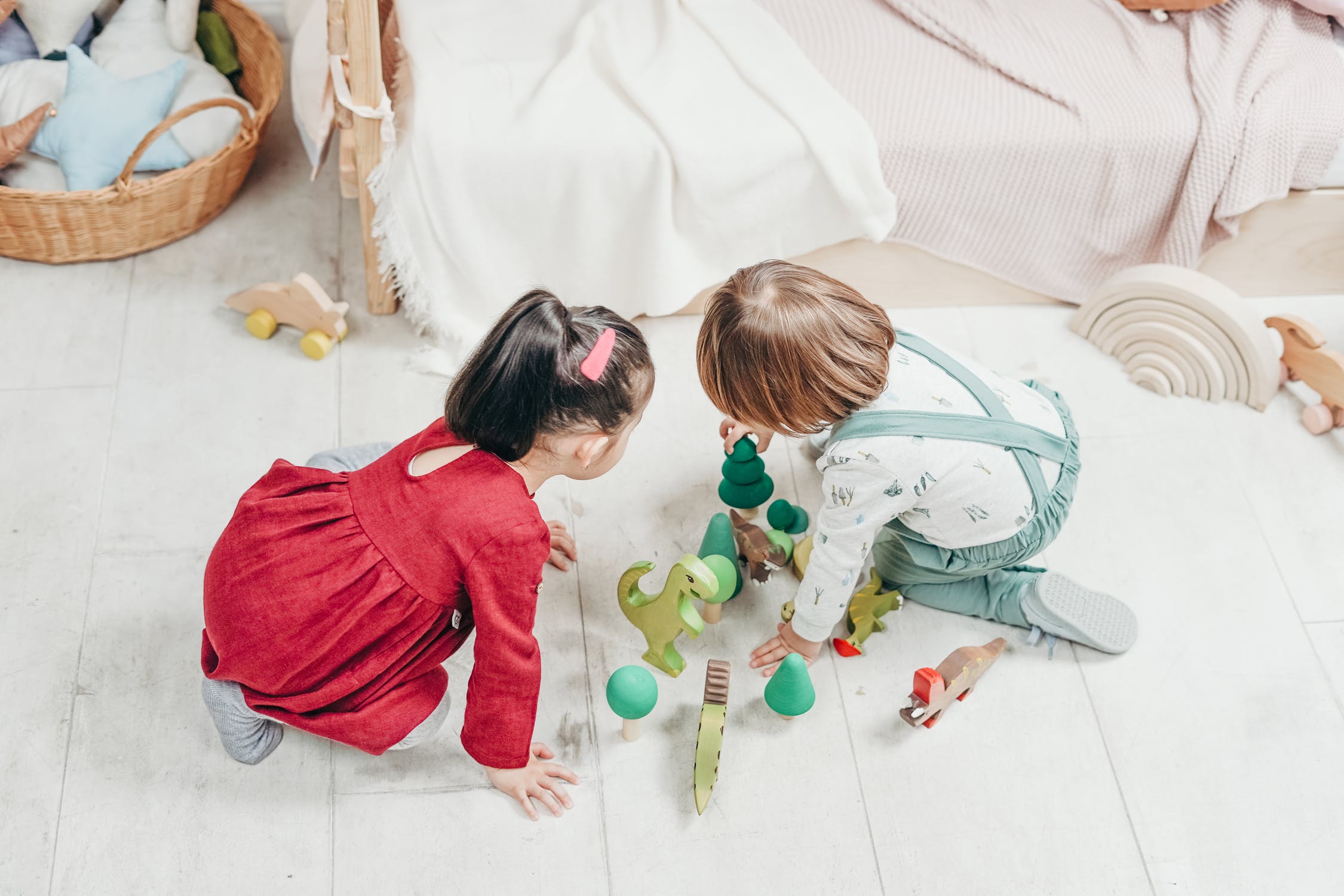 Two girls playing on the floor with green toys such as dinosaurs