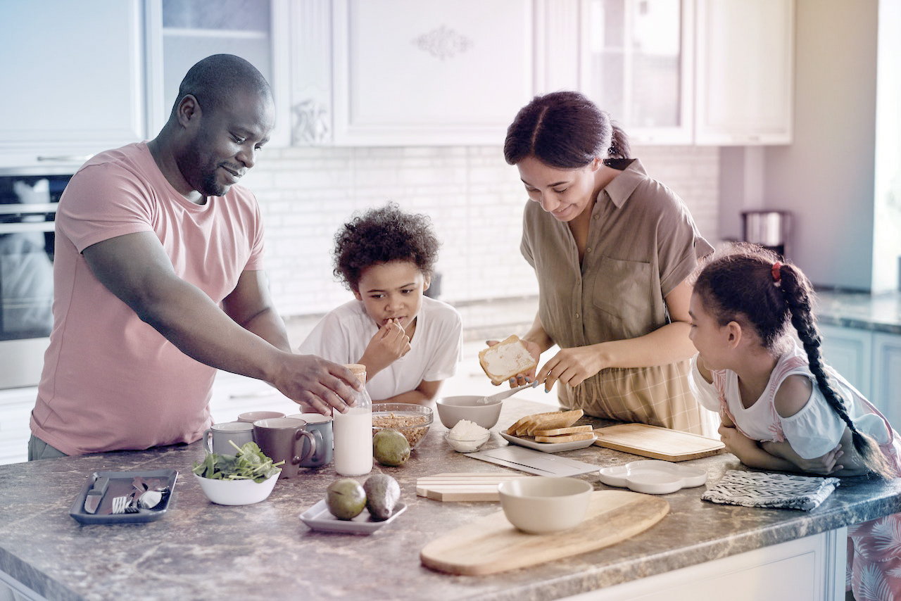 "Stock image of man, woman, two children gathered around kitchen island with wooden countertop, preparing meal with sliced bread."