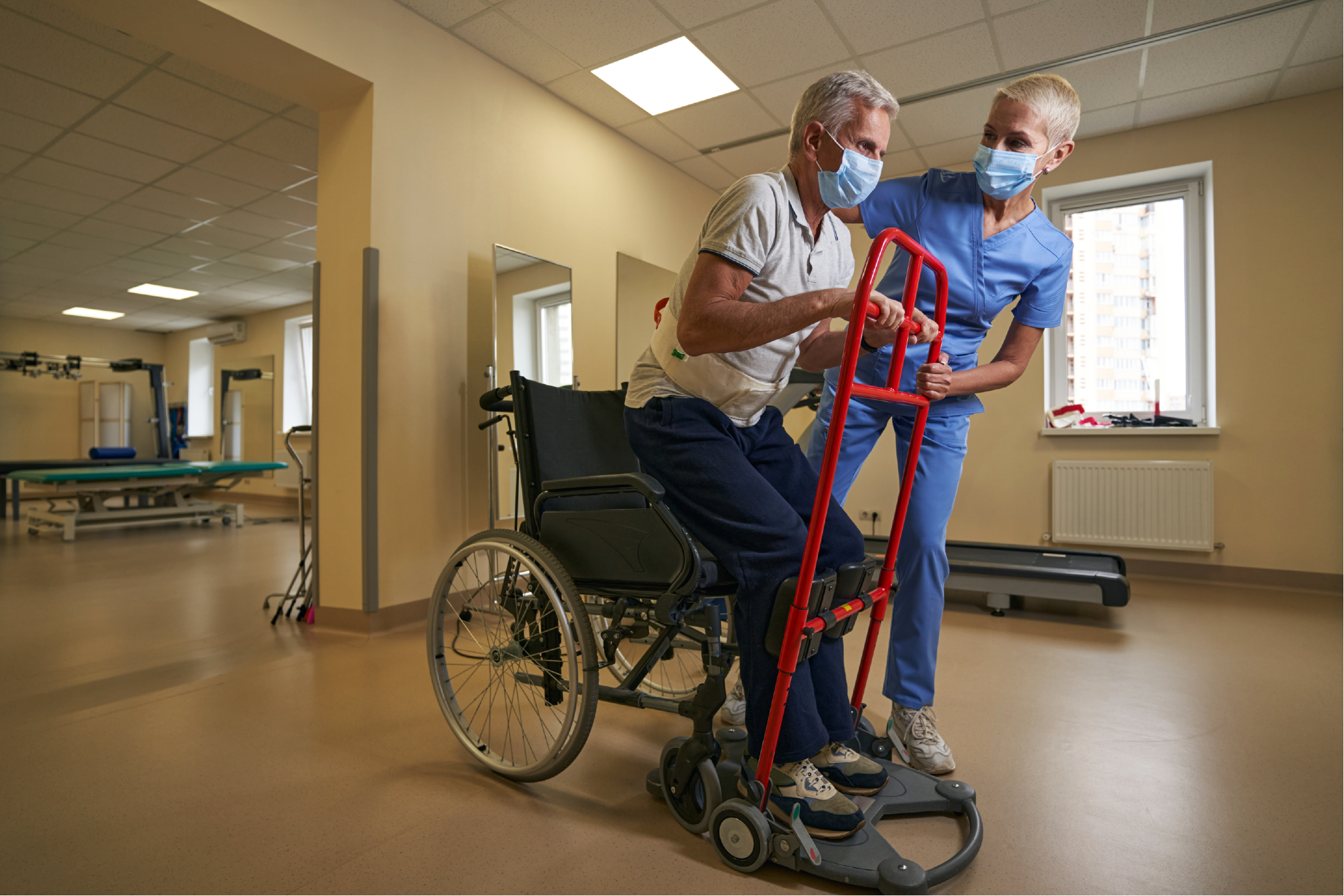 "A physical therapist helps a stroke patient in rehab center while both wear masks during covid"