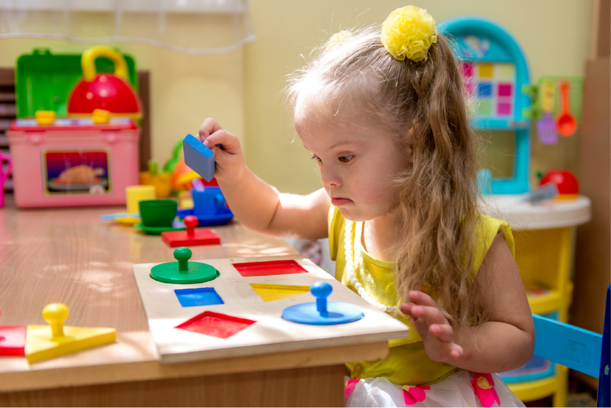 "A preschool girl with Down Syndrome plays with a puzzle in a classroom environment"