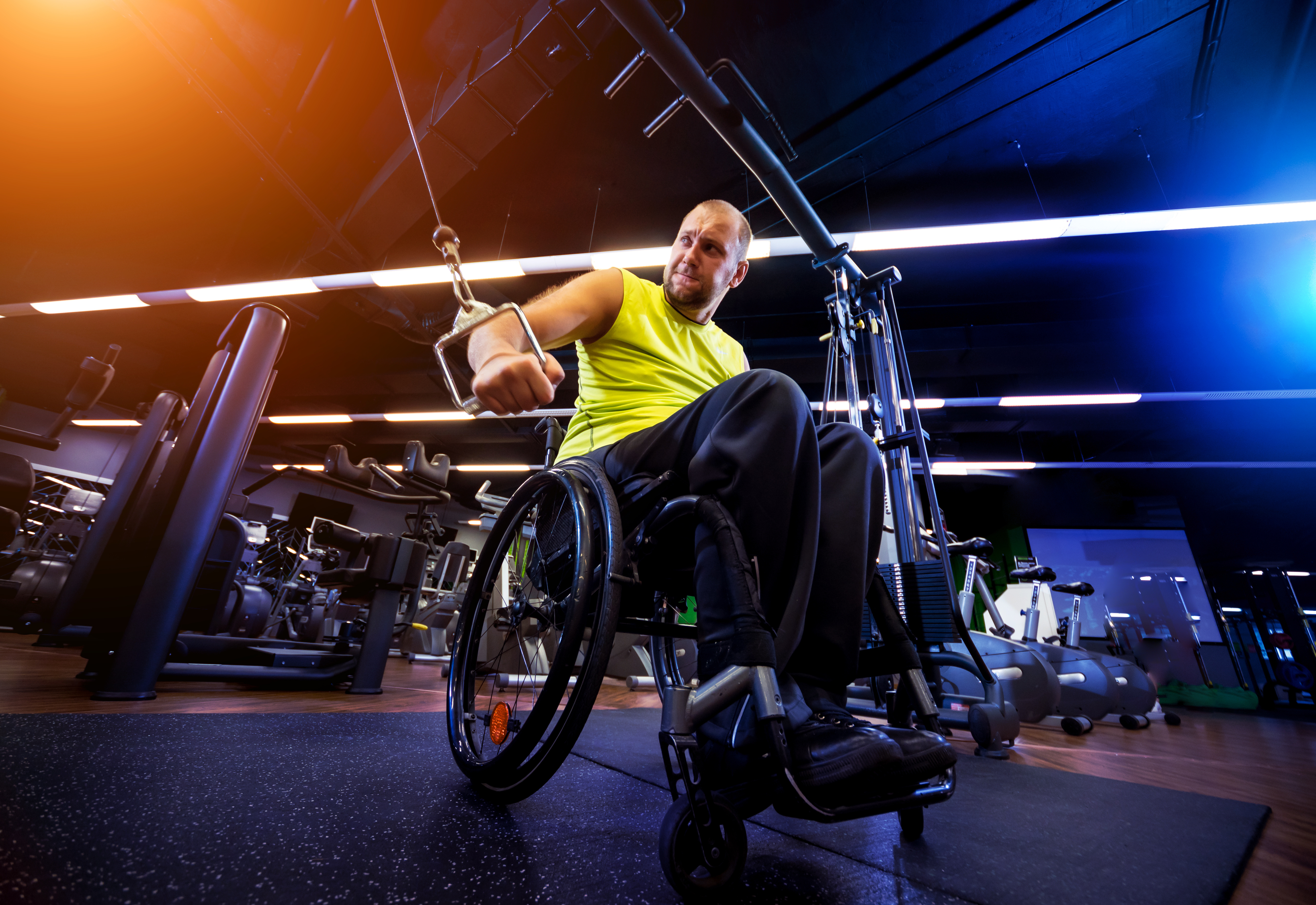 "A man sitting in a wheelchair uses an exercise machine at a gym"