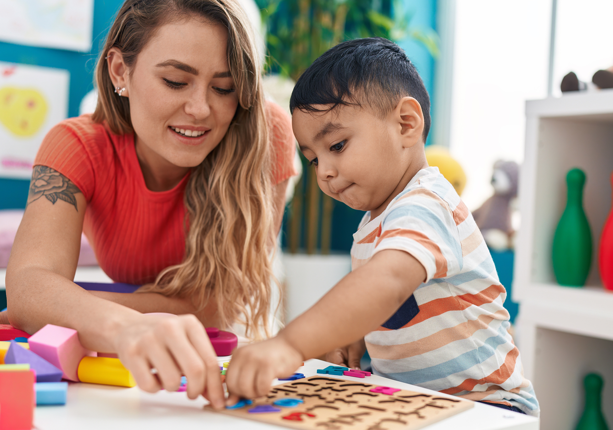 "A woman interacts with a young child while putting a puzzle together in a classroom setting"