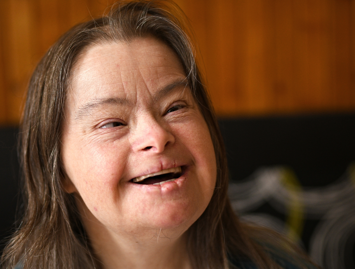 "A woman with Down syndrome with gray highlights in her long brown hair smiles"