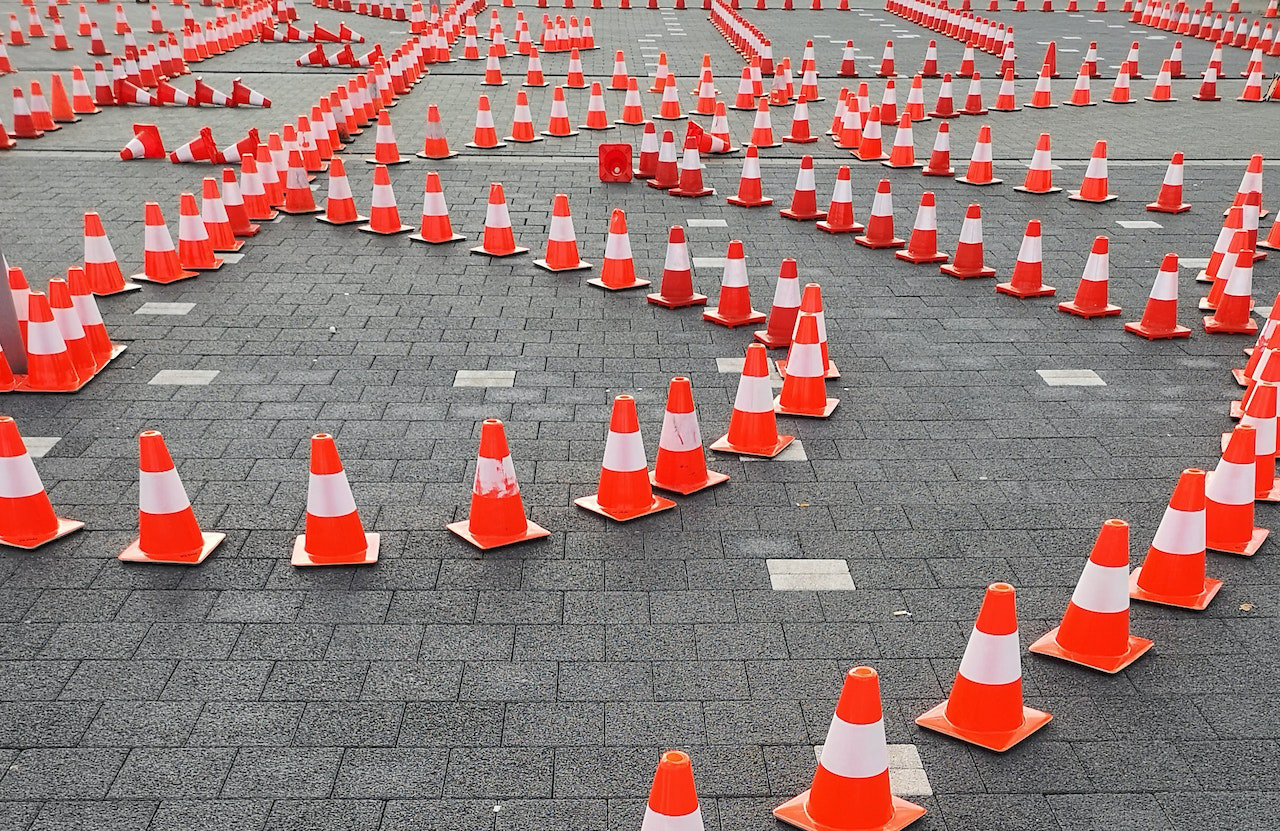 "Dozens or bright orange traffic cones are lined up in rows along a concrete surface"