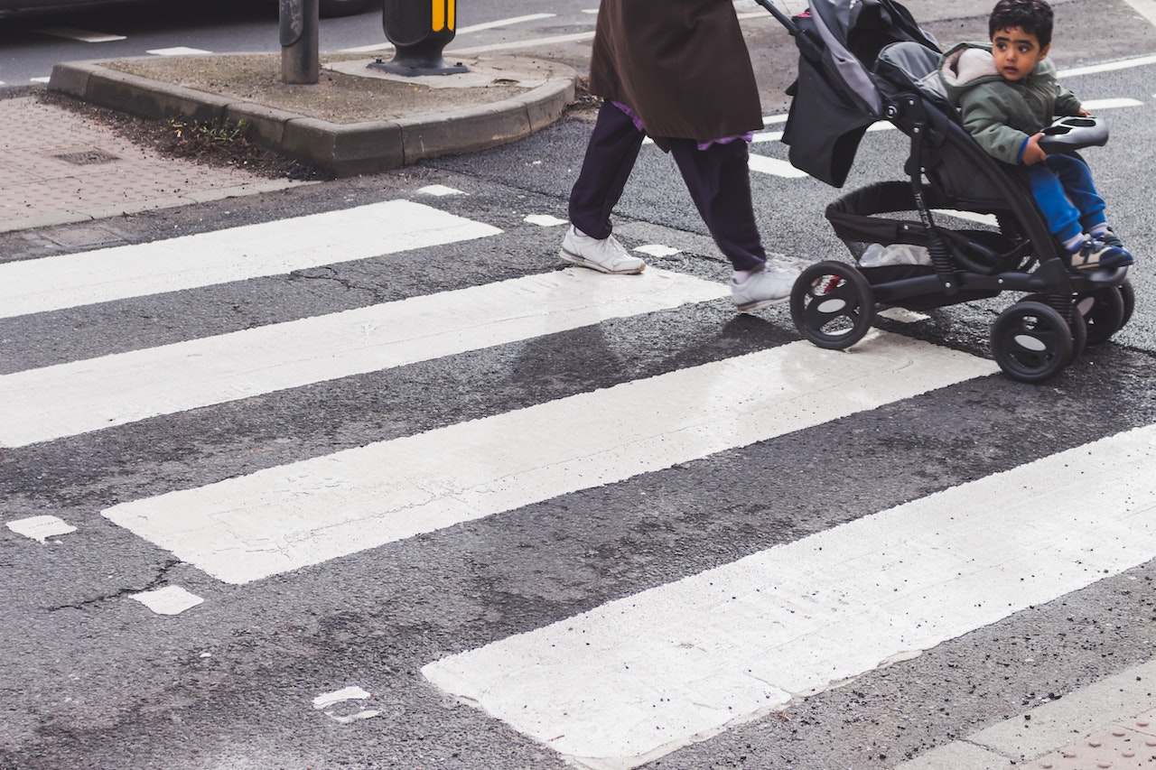 "A woman pushes a young child in a stroller across a crosswalk past"