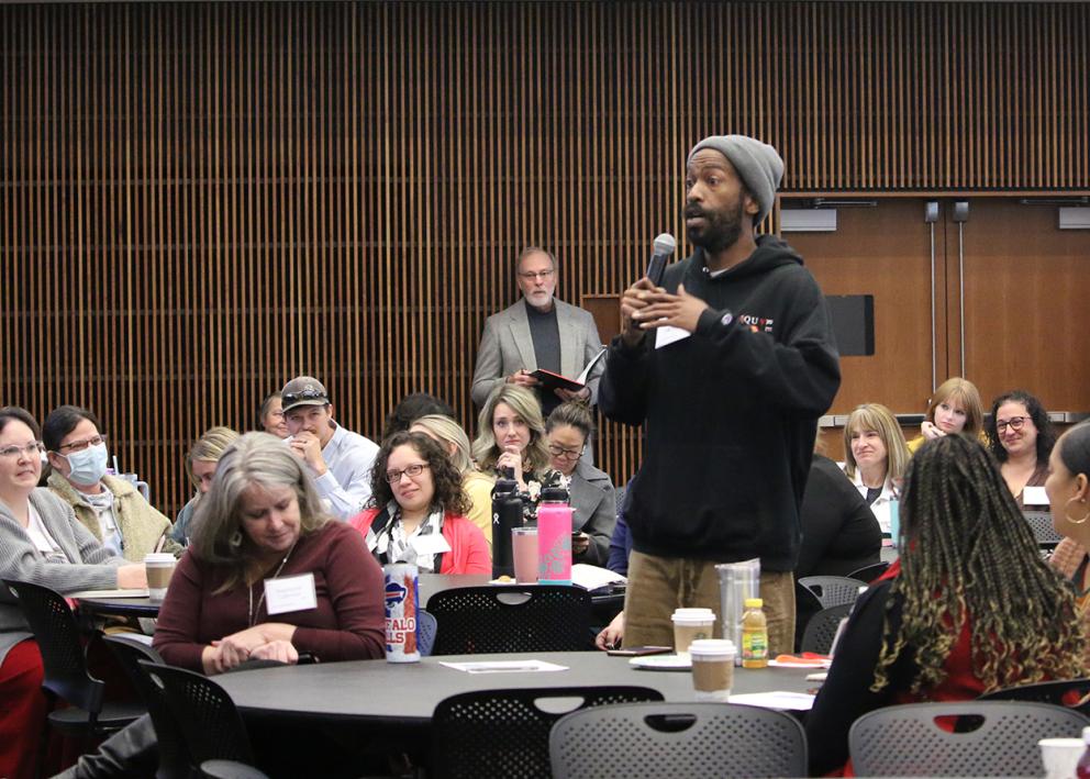 A man in the audience stands and speaks into a microphone to address the room