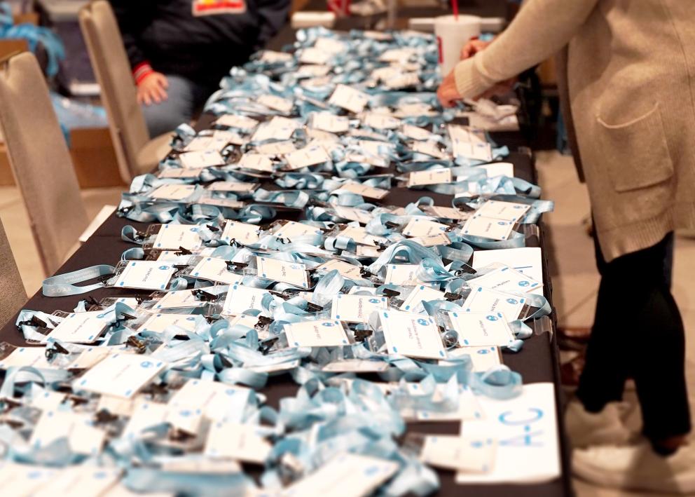 Hundreds of name tags with lanyards are spread on a black table as a person sorts through them