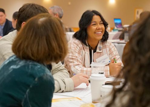 A woman smiles as she listens to discussions at her table with others at the 2023 Life Span Institute Collaboratory