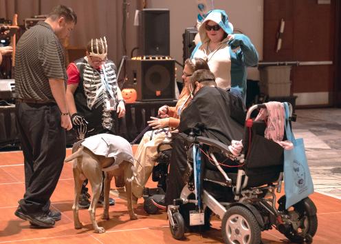 Five people stand or sit in wheelchairs in a circle and talk, with some of them wearing costumes