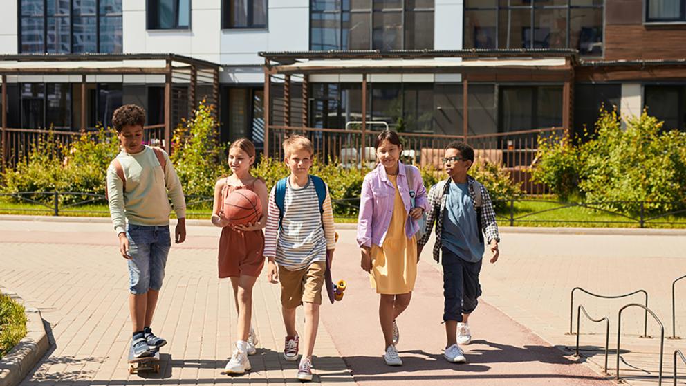 A group of five children walking outside a school on a sunny day